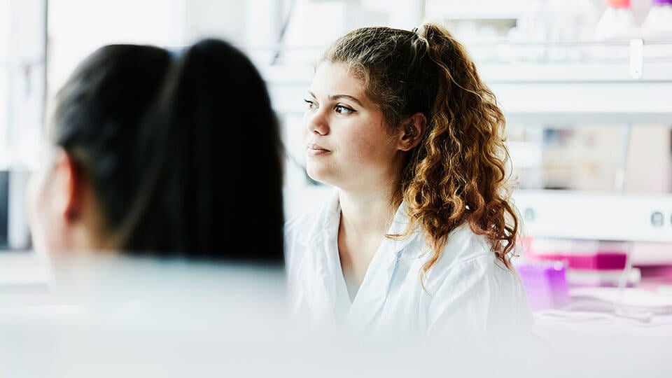 Smiling female scientist listening during project discussion with colleagues in laboratory