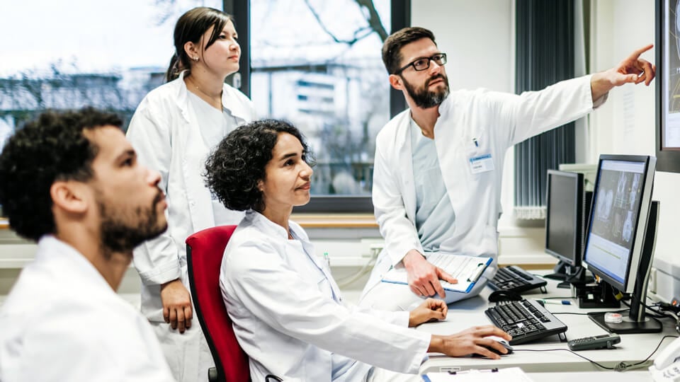 A team of doctors looking at some lab results together on monitors, in an office at the hospital.