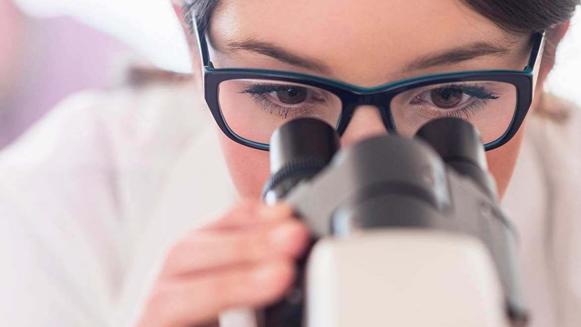 Young female scientist looking through microscope