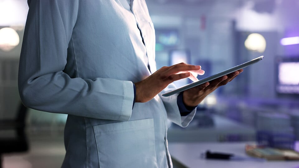 A scientist in a lab coat holding a tablet, engaged in scientific research or data analysis